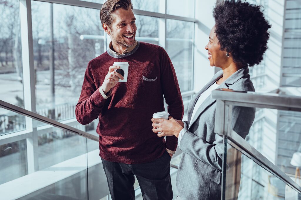Two business professionals engaged in an attentive conversation on an office staircase, illustrating listening without judgment as a leadership skill.
