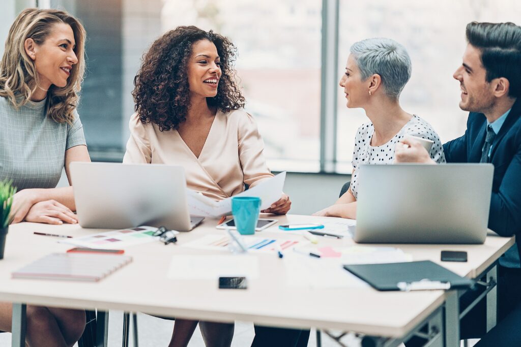 Four professionals seated around a conference table in discussion, representing leadership communication, collaboration and human connection in an AI-enabled workplace.